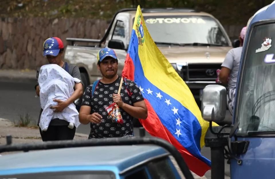 A Venezuelan migrant trying to reach the United States, carries a national flag as he walks with a woman and a baby along a road in Tegucigalpa, Honduras, on September 19, 2023. (Photo by Orlando SIERRA / AFP)